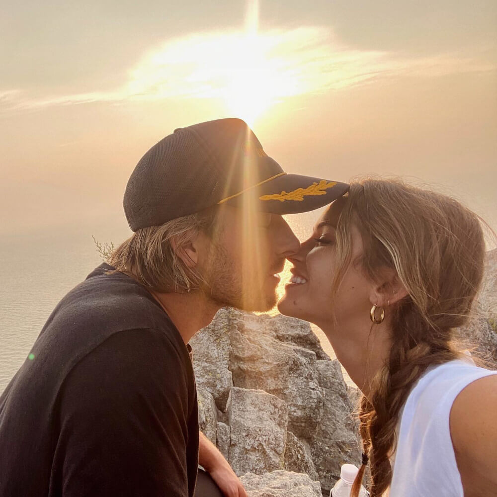 Glen Powell and Gigi Paris kissing in front of the sunset